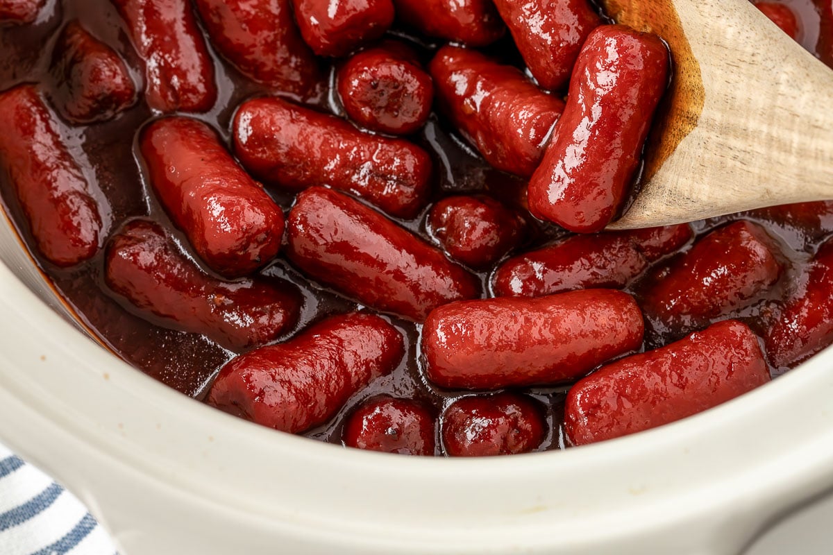 Little smokies simmering in a slow cooker with grape jelly and chili sauce.