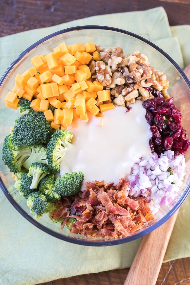 chopped vegetables, nuts, cheese, onions and bacon with dressing in a bowl