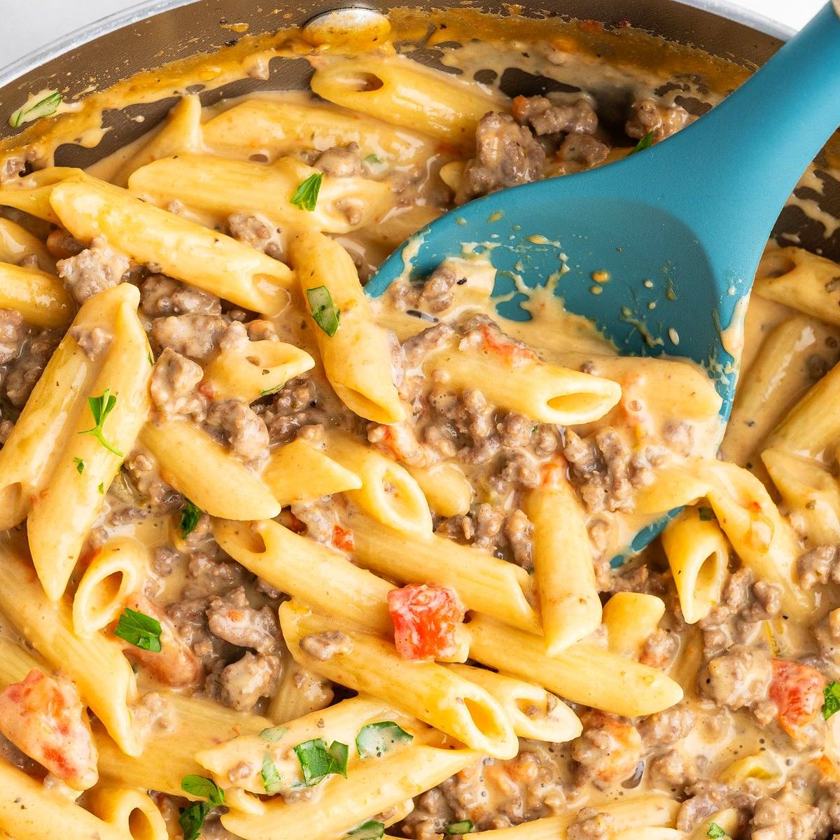 Creamy Rotel pasta with ground beef on a blue spoon in the skillet