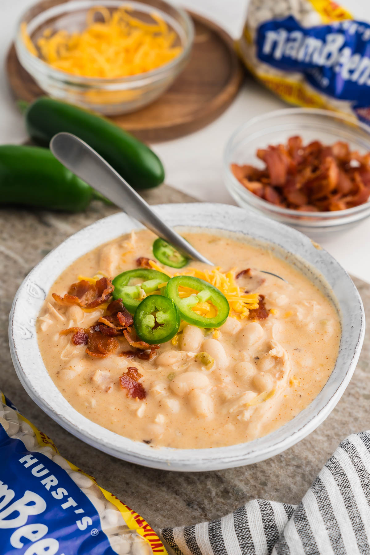 Serving of white chicken chili with jalapeños, bacon pieces, and fresh herbs on top.
