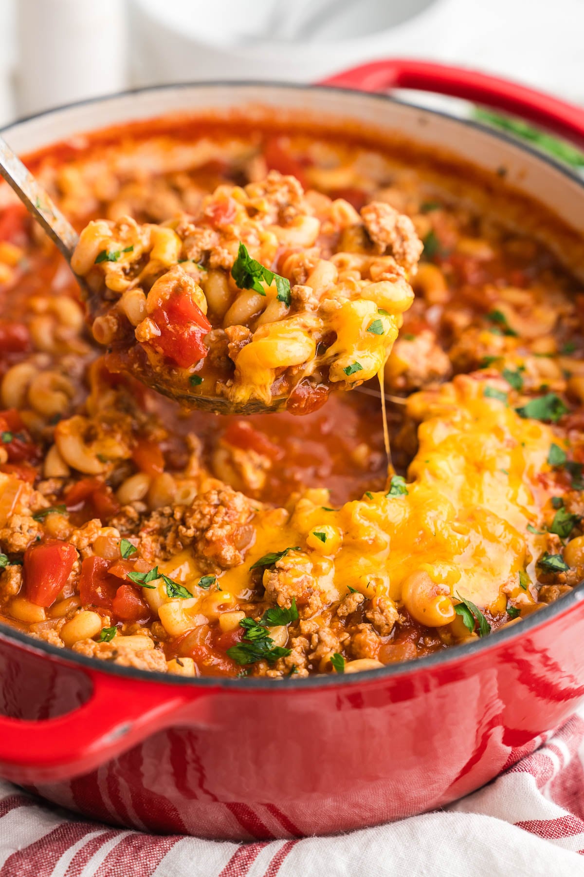 Spoonful of cheesy macaroni in tomato sauce lifted from the pot