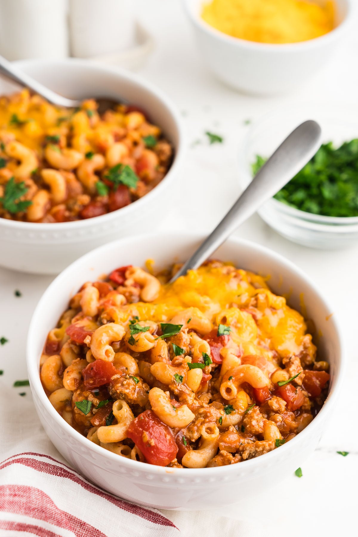 Two bowls of easy ground turkey goulash with shredded cheddar on top