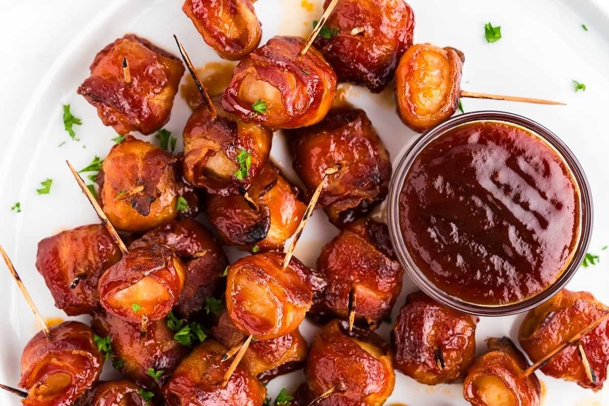 Bacon wrapped water chestnuts with toothpicks around a bowl of sticky brown sugar sauce