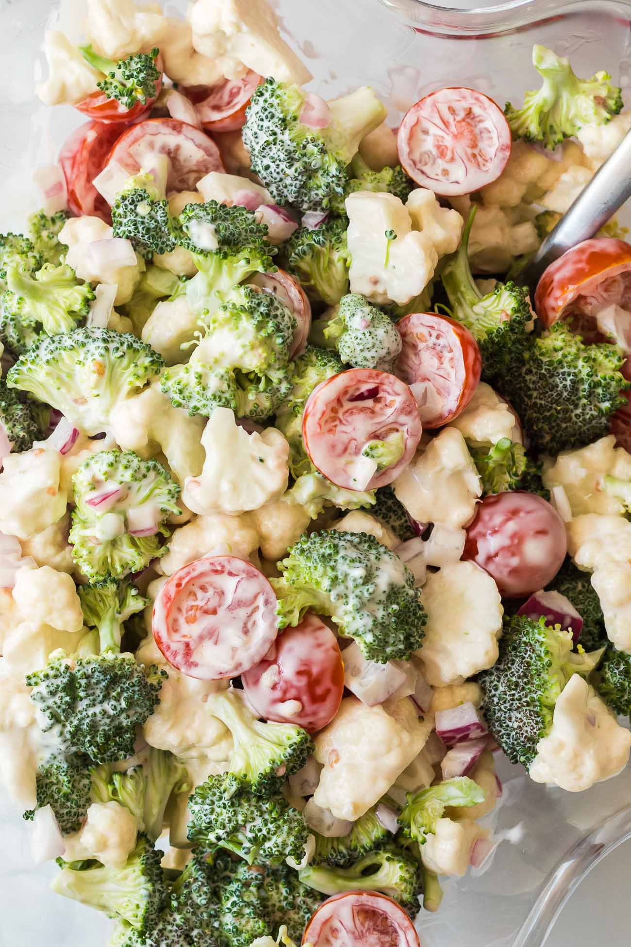 Close-up of broccoli, cauliflower and halved cherry tomatoes coated in a creamy dressing