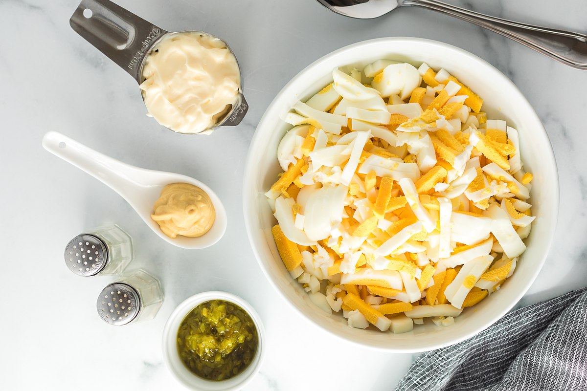 Overhead view of a white bowl of chopped whites and yolks with mayo, dill pickle relish, Dijon mustard, salt and pepper.