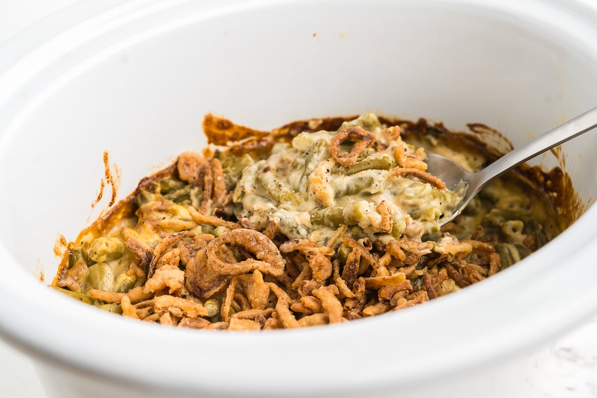Spoonful of creamy green beans and crunchy fried onions lifted from the crock pot
