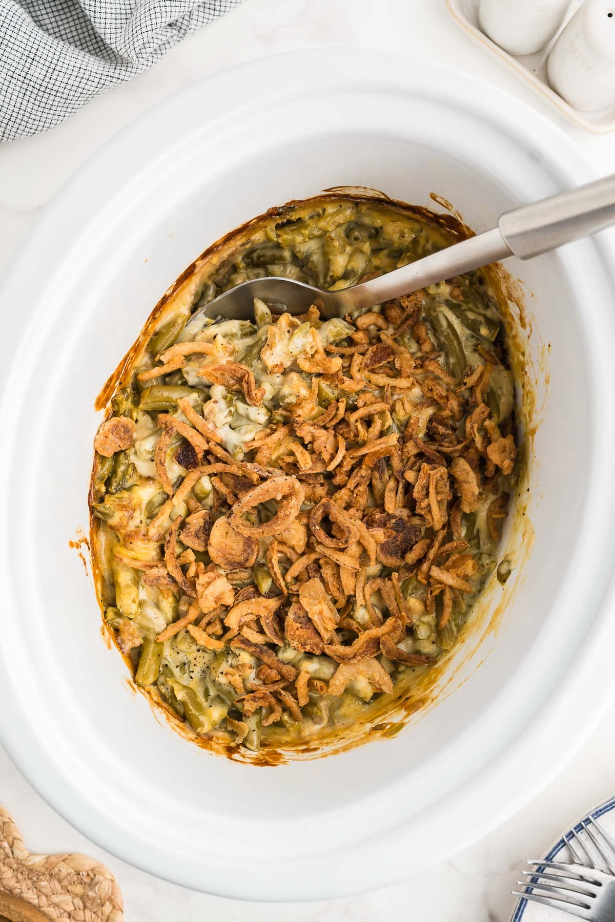 Serving spoon in a crockpot green bean casserole with a golden fried onion topping