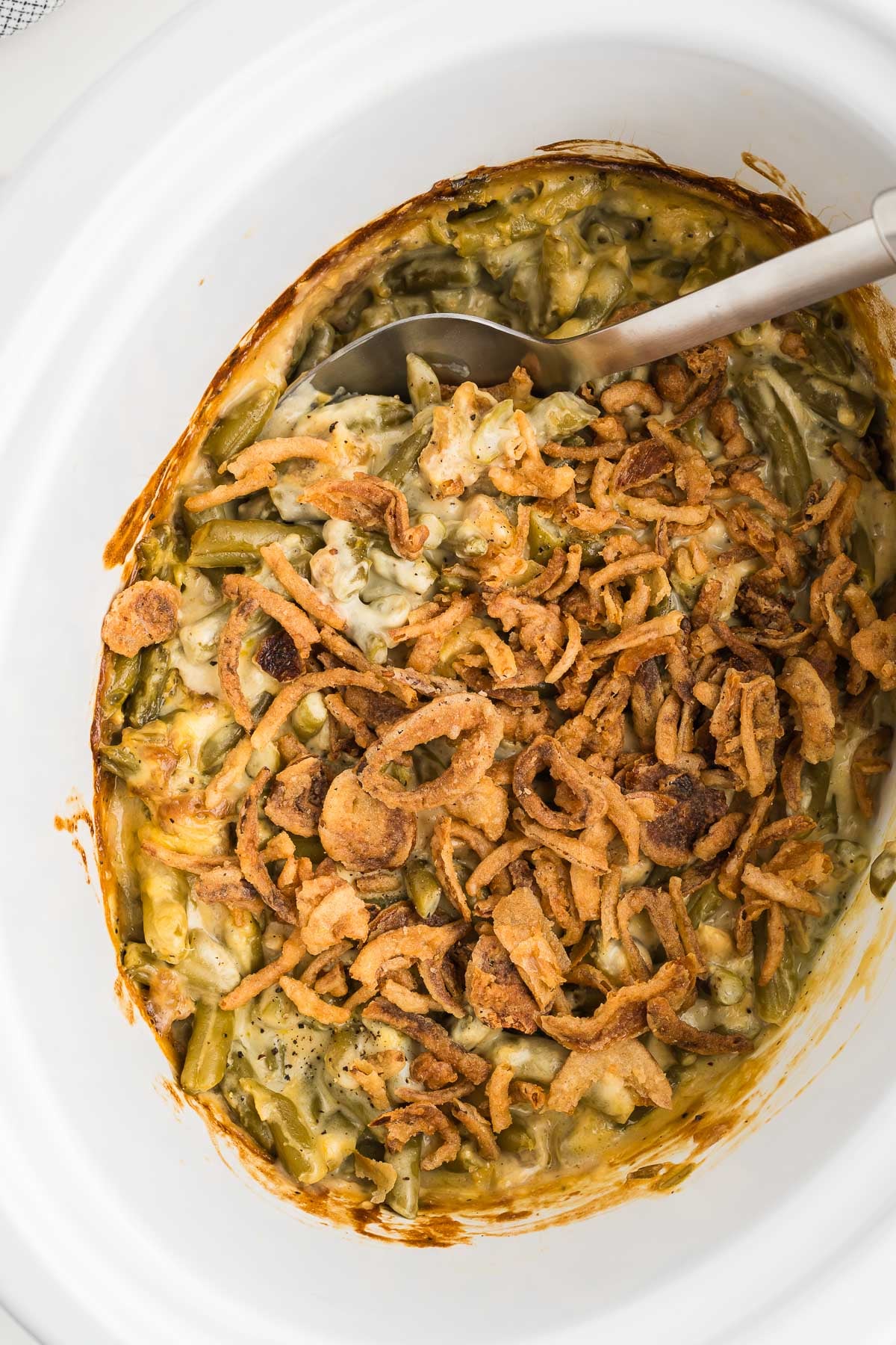 Close-up of creamy green beans under golden fried onions, finished in the slow cooker