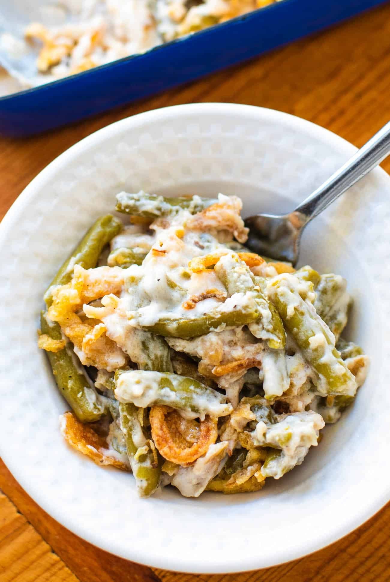 A white bowl of creamy canned green beans with crunchy onions and a spoon