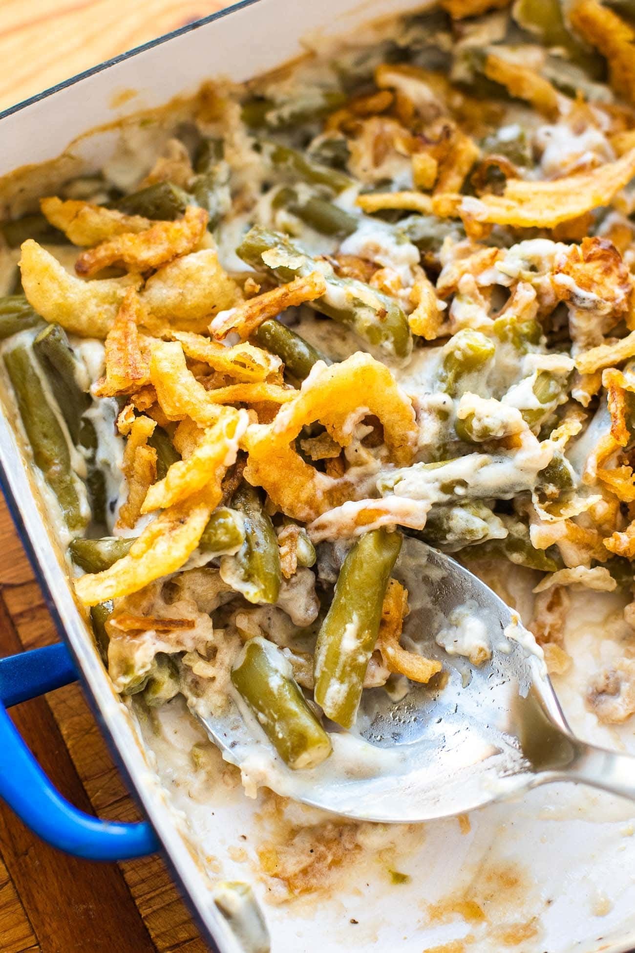 A serving spoon lifting creamy green beans and fried onions out of the baking dish
