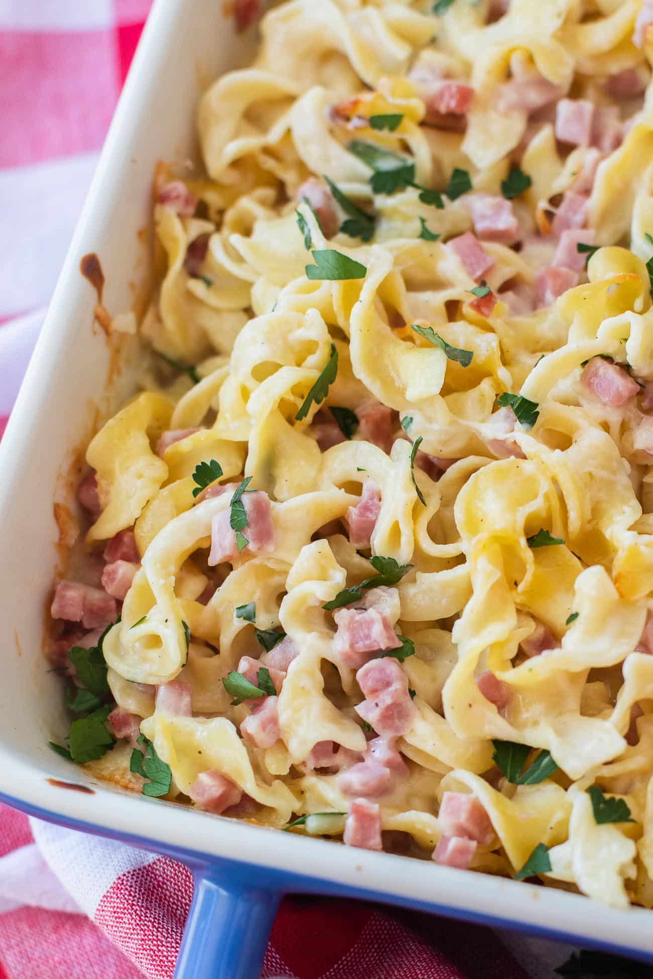 Cheesy pasta bake with fresh parsley in a white baking dish on a red checkered towel