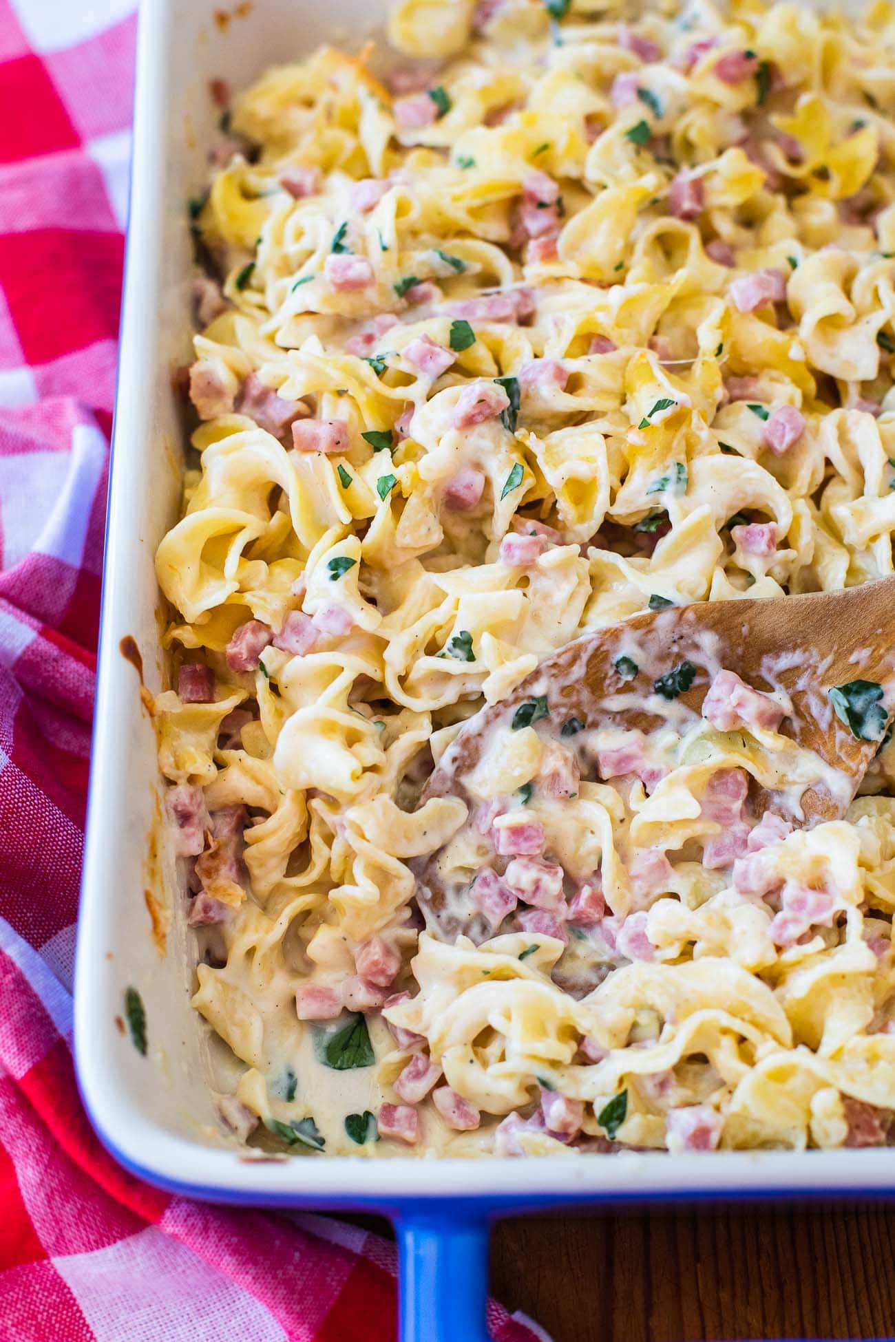 Creamy pasta bake with fresh parsley in a white dish with a wooden spoon