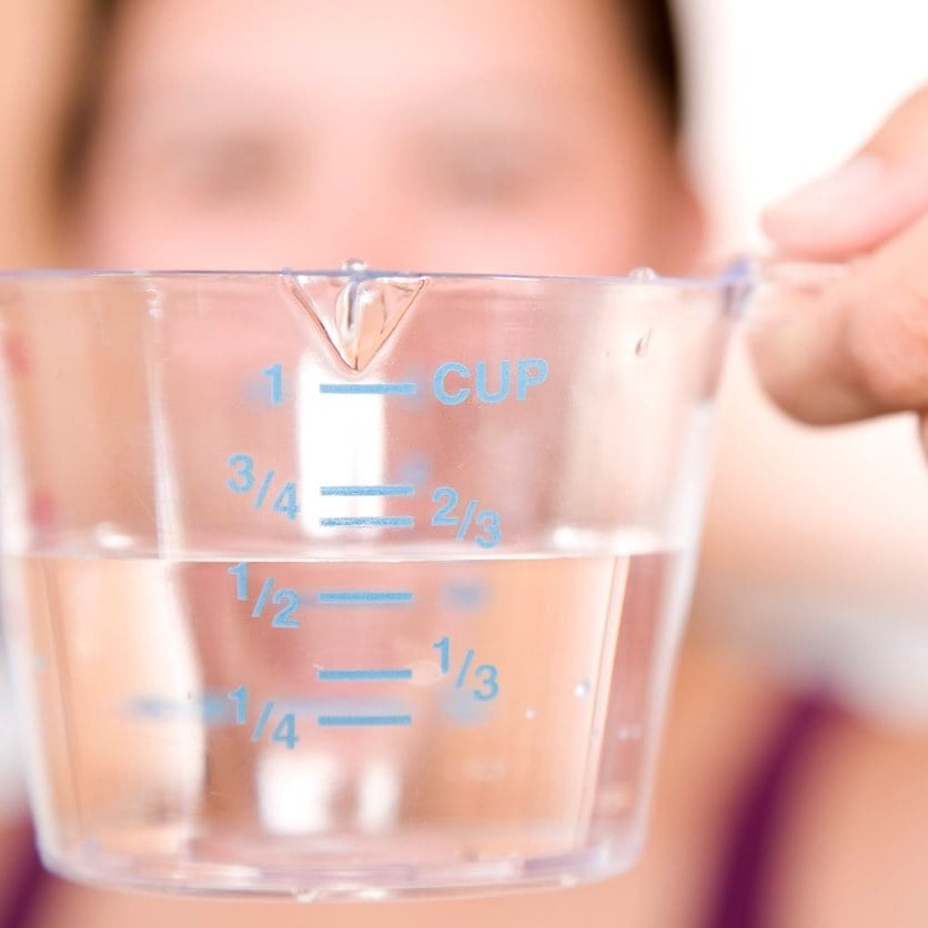 A hand holding a glass measuring cup filled with water