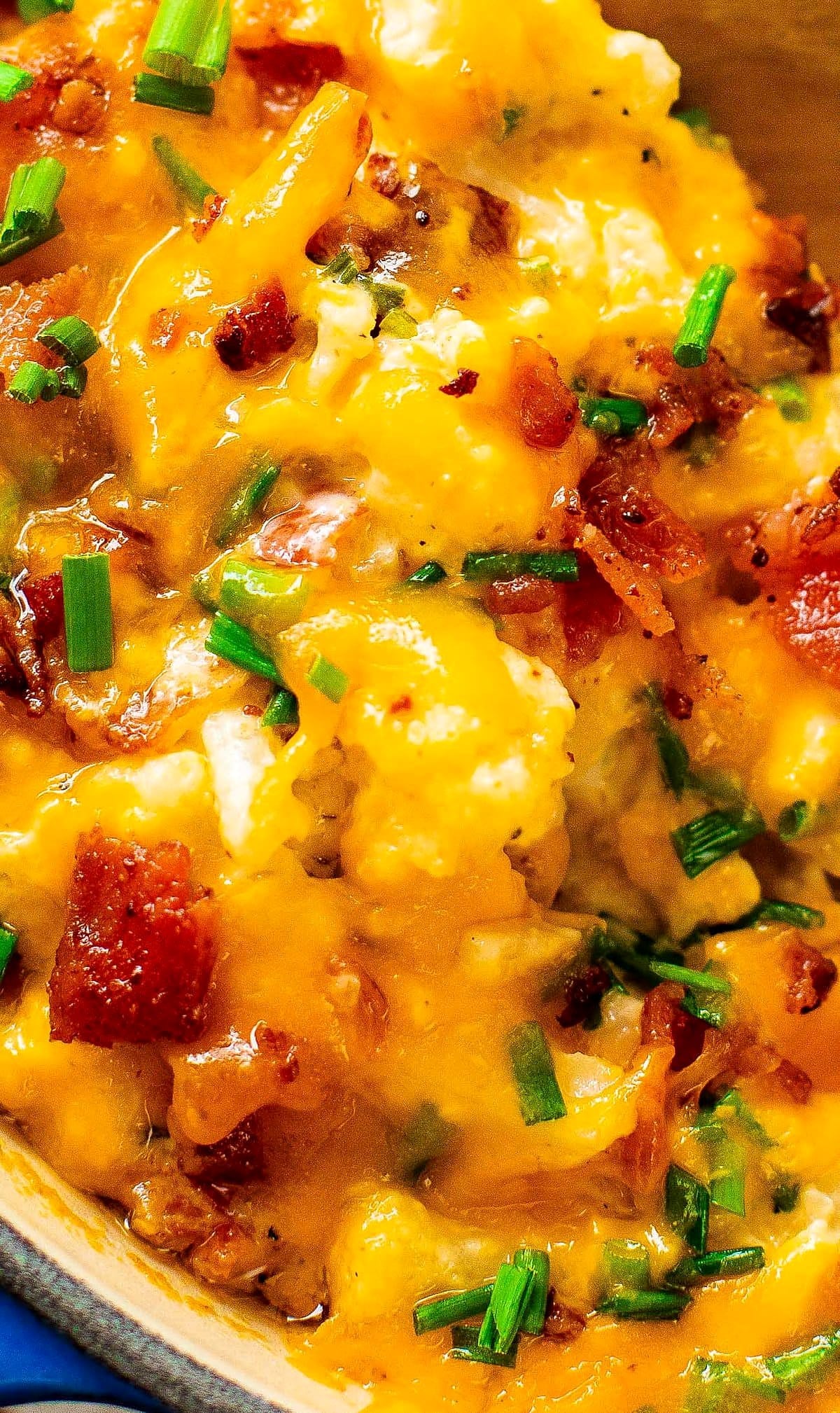 Close-up of bubbly cheddar cheese, crumbled bacon and chives on top of the casserole.
