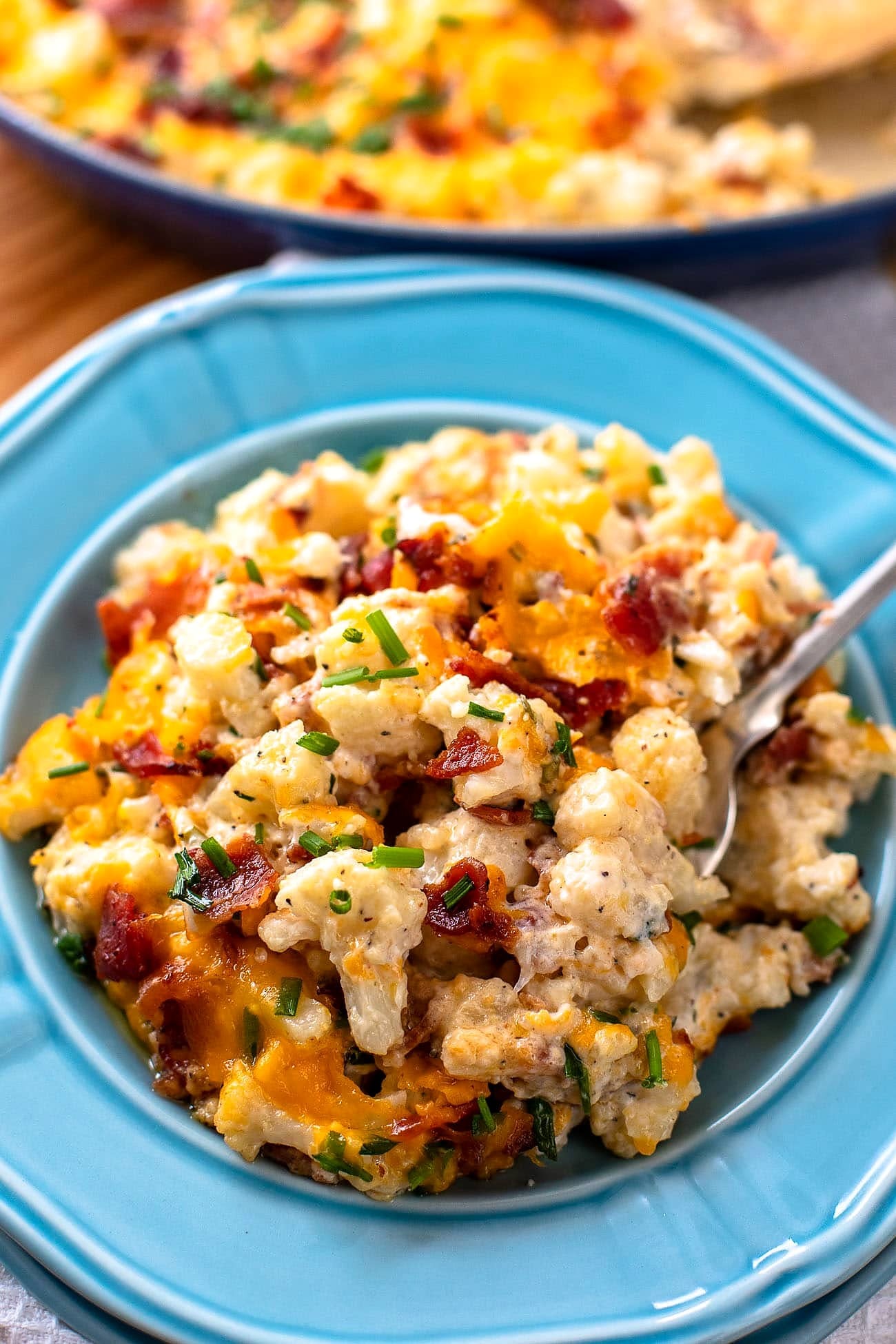 A serving of loaded cauliflower casserole on a blue plate with a fork.