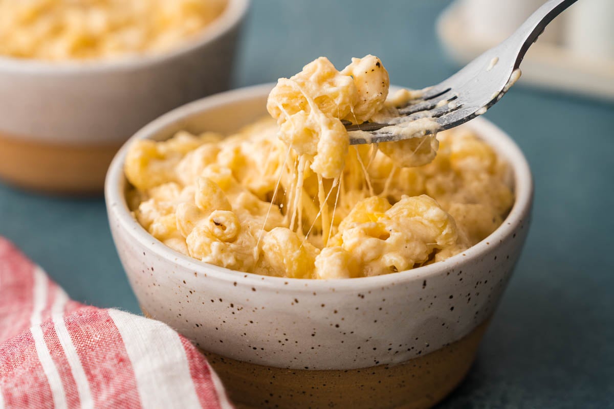 Fork lifting creamy pasta from a speckled bowl with strands stretching below.
