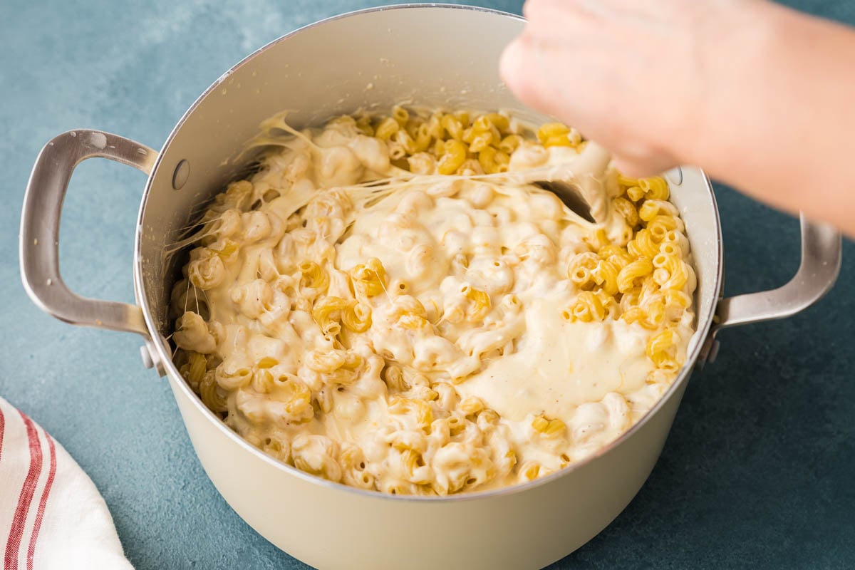 Spoon pulling stretchy melted sauce through pasta in a large pot.