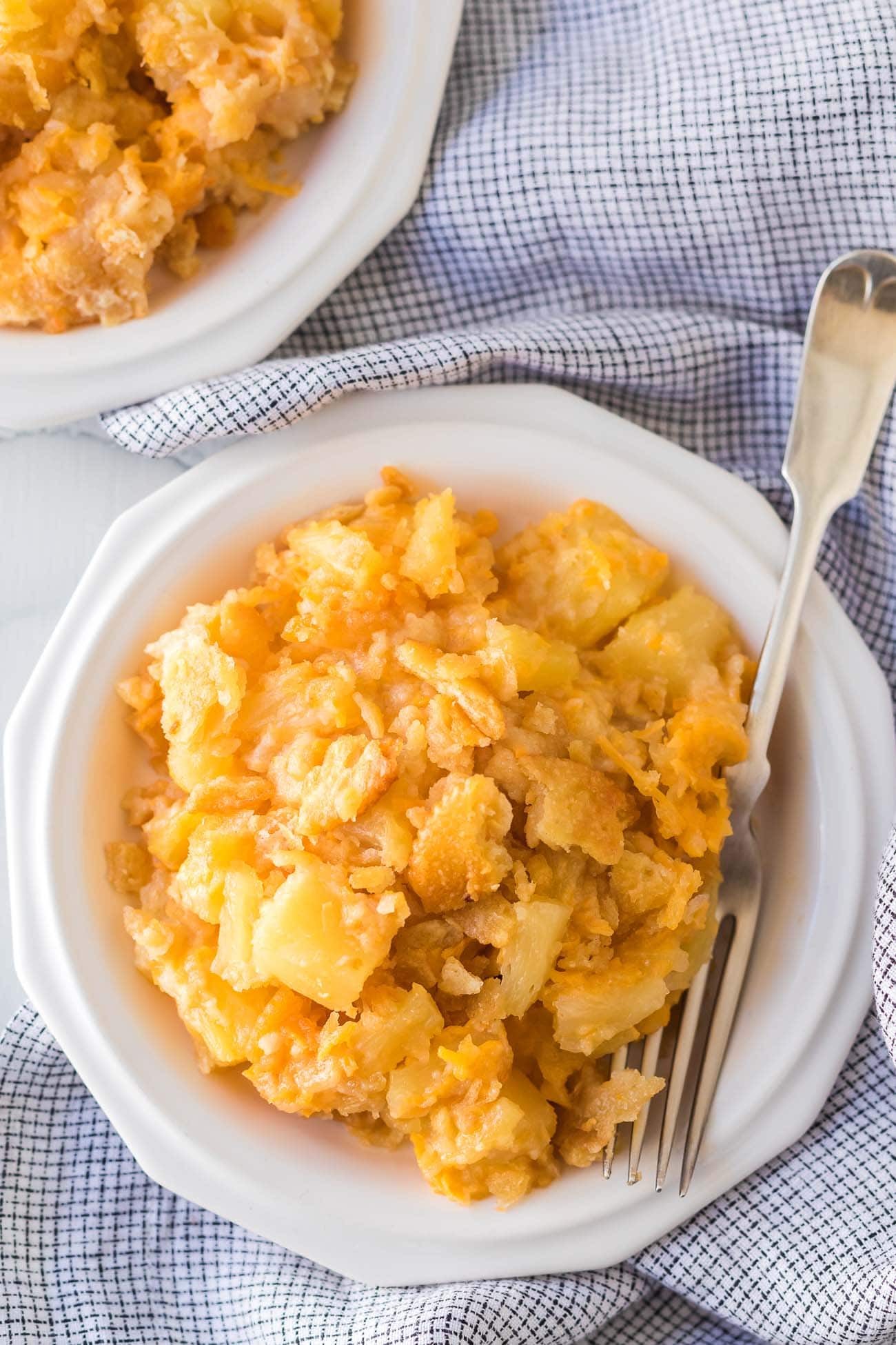 A cheesy serving with a buttery cracker topping on a white plate with a fork