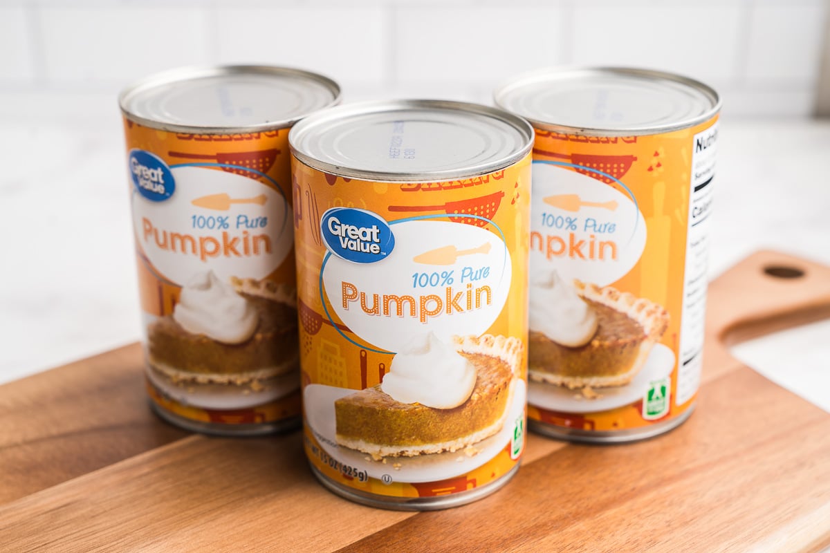 Three unopened cans of pure pumpkin on a wooden cutting board