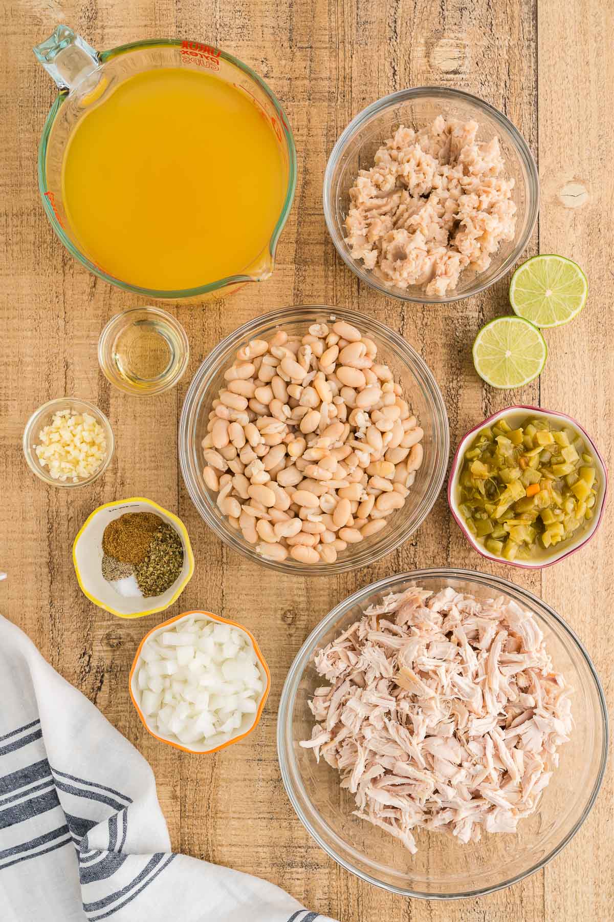 Ingredients laid out in glass bowls: broth, great northern beans, diced green chiles, onion, garlic, spices and limes