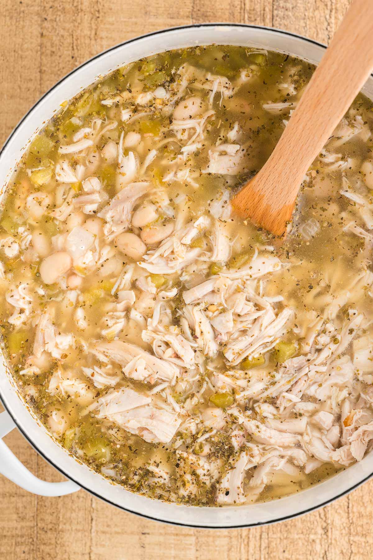 Close-up of the creamy broth and great northern beans in the pot with a wooden spoon