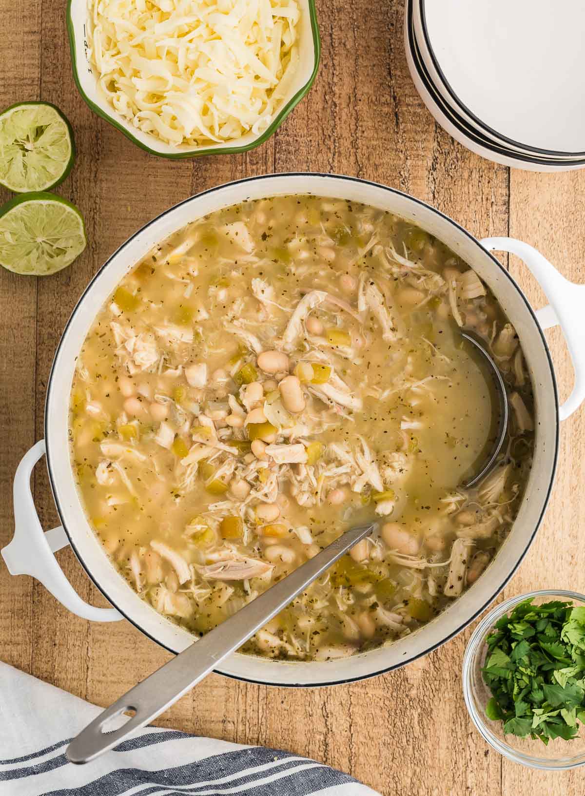 Dutch oven of white chicken chili with shredded chicken and white beans, with limes and shredded cheese on the side